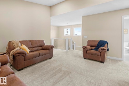 Carpeted loft area with light neutral wall paint, white railings, and two transom windows - 7135 Edgemont Way Nw, Edmonton, AB 