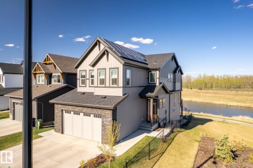 Contemporary exterior design featuring a stone-clad garage, solar panels, and a concrete driveway - 7135 Edgemont Way Nw, Edmonton, AB 