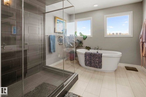 Freestanding soaking tub, walk-in shower with glass enclosure, wood-finish flooring, and dual windows - 7135 Edgemont Way Nw, Edmonton, AB 