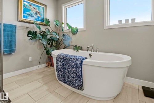 Freestanding soaking tub with chrome fixtures, set against light gray walls with rectangular tile flooring - 7135 Edgemont Way Nw, Edmonton, AB 