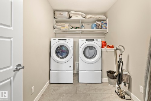 Built-in shelving units, light-toned wall paint, modern front-loading washer and dryer units, and light grey floor tiling - 7135 Edgemont Way Nw, Edmonton, AB 