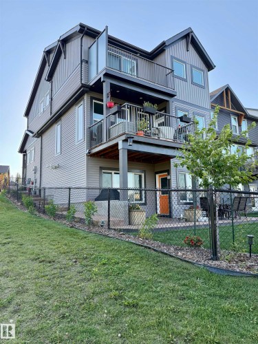 Multi-story exterior featuring two balconies, a ground-level patio, and a sloped yard with fencing - 7135 Edgemont Way Nw, Edmonton, AB 