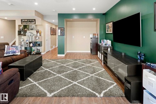 Wood-finish flooring, recessed lighting, and a green accent wall with a built-in media console - 7135 Edgemont Way Nw, Edmonton, AB 