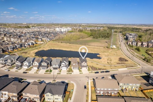 Established residential area with a prominent water feature, surrounded by natural landscaping and adjacent to a paved road - 7135 Edgemont Way Nw, Edmonton, AB 