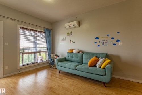 Light-toned wood-finish flooring enhances this room featuring a large window with blinds and a wall-mounted air conditioning unit - #407 9523 160 Av Nw, Edmonton, AB - Indoor Photo Showing Living Room