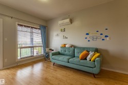 Light-toned wood-finish flooring enhances this room featuring a large window with blinds and a wall-mounted air conditioning unit - 