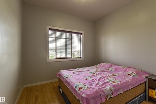 Bedroom featuring wood-finish flooring, a window with horizontal blinds, and neutral-toned walls - #407 9523 160 Av Nw, Edmonton, AB - Indoor Photo Showing Bedroom
