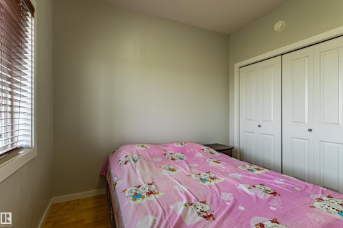 Bedroom featuring light-toned walls, wood-finish flooring, a window with horizontal blinds, and a built-in double closet with white bi-fold doors - #407 9523 160 Av Nw, Edmonton, AB - Indoor Photo Showing Bedroom