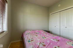 Bedroom featuring light-toned walls, wood-finish flooring, a window with horizontal blinds, and a built-in double closet with white bi-fold doors - 