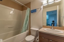 Bathroom featuring a white tub/shower combination, toilet, and vanity with a built-in sink and wood-finish cabinetry - 
