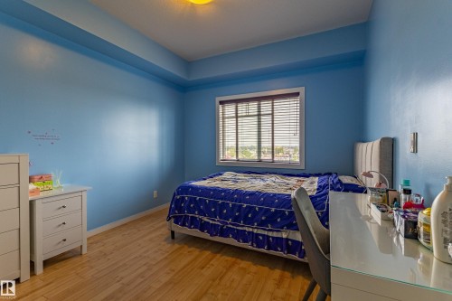 Room featuring wood-finish flooring, a window with horizontal blinds, and crown molding - #407 9523 160 Av Nw, Edmonton, AB - Indoor Photo Showing Bedroom
