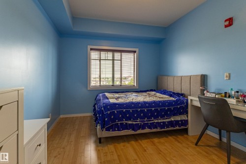 Room featuring wood-finish flooring, a window with horizontal blinds, and a built-in soffit - #407 9523 160 Av Nw, Edmonton, AB - Indoor Photo Showing Bedroom