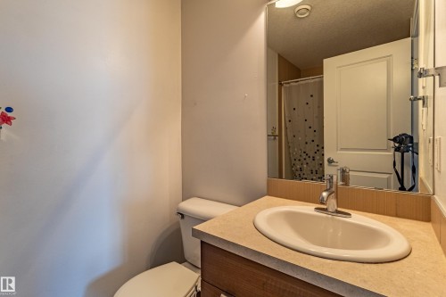 Bathroom featuring an integrated sink, laminate countertop, wood-finish vanity, and wall-mounted mirror - #407 9523 160 Av Nw, Edmonton, AB - Indoor Photo Showing Bathroom