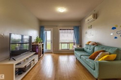 Bright living area featuring wood-finish flooring, a wall-mounted air conditioning unit, and a glass-paneled door leading to an outdoor space - 
