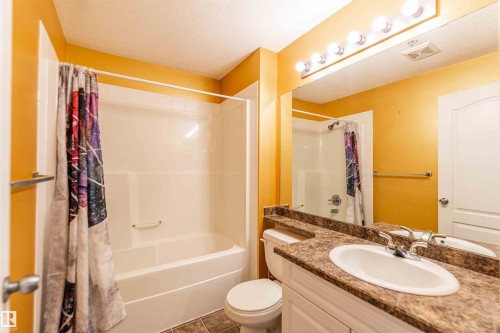 This bathroom features a white bathtub and shower combination, a vanity with a countertop, an undermount sink, and a large mirror with overhead lighting - #1111 7339 South Terwillegar Dr Nw, Edmonton, AB - Indoor Photo Showing Bathroom