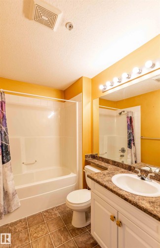 Bathroom featuring a white vanity with a countertop, an integrated sink, and a large mirror with vanity lighting - #1111 7339 South Terwillegar Dr Nw, Edmonton, AB - Indoor Photo Showing Bathroom