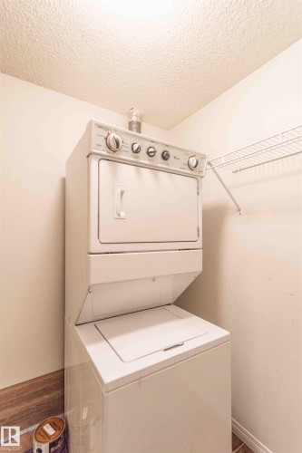 Laundry area featuring a stacked washer and dryer unit and a wire shelf for storage - #1111 7339 South Terwillegar Dr Nw, Edmonton, AB - Indoor Photo Showing Laundry Room