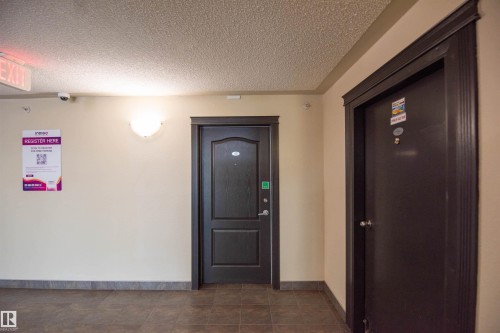 The property features a dark wood door with decorative molding, set within a light-colored hallway with tiled flooring - #1111 7339 South Terwillegar Dr Nw, Edmonton, AB - Indoor Photo Showing Other Room