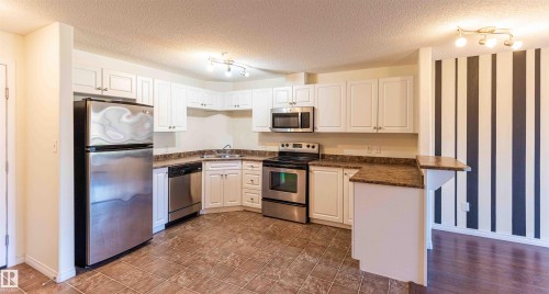 The kitchen features white cabinetry, stainless steel appliances, and brown tiled flooring - #1111 7339 South Terwillegar Dr Nw, Edmonton, AB - Indoor Photo Showing Kitchen With Stainless Steel Kitchen