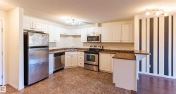 The kitchen features white cabinetry, stainless steel appliances, and brown tiled flooring - 