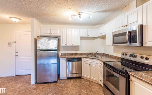 The kitchen features white cabinetry, stone-look countertops, and stainless steel appliances including a refrigerator, dishwasher, microwave, and stove - #1111 7339 South Terwillegar Dr Nw, Edmonton, AB - Indoor Photo Showing Kitchen With Stainless Steel Kitchen With Double Sink
