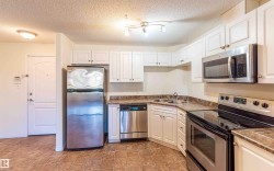 The kitchen features white cabinetry, stone-look countertops, and stainless steel appliances including a refrigerator, dishwasher, microwave, and stove - 