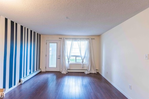 This room features dark hardwood flooring, a window with curtains, and a glass-paneled door - #1111 7339 South Terwillegar Dr Nw, Edmonton, AB - Indoor Photo Showing Other Room