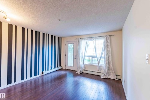This space features dark hardwood flooring, a window with sheer curtains, and a door with a glass panel - #1111 7339 South Terwillegar Dr Nw, Edmonton, AB - Indoor Photo Showing Other Room