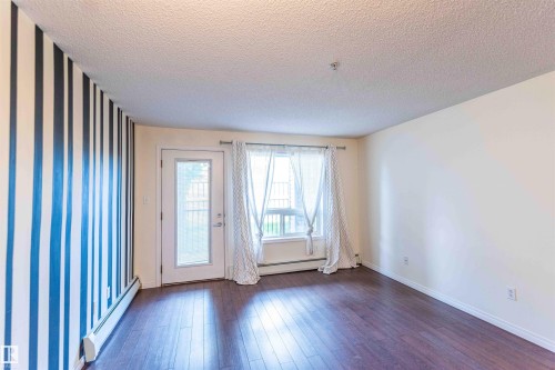 This living area features rich dark flooring, a white ceiling, and a wall with a distinctive vertical stripe pattern - #1111 7339 South Terwillegar Dr Nw, Edmonton, AB - Indoor Photo Showing Other Room