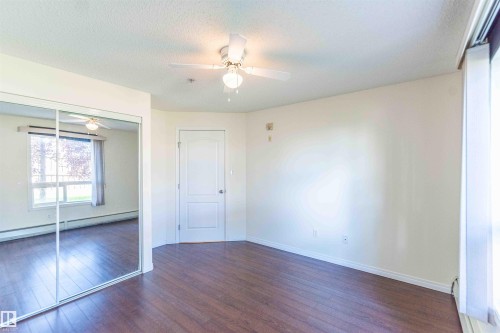 The property offers a room with dark wood flooring, a white ceiling fan, and large mirrored closet doors - #1111 7339 South Terwillegar Dr Nw, Edmonton, AB - Indoor Photo Showing Other Room