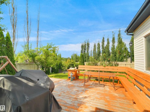 Expansive wooden deck with built-in bench seating, overlooking a manicured lawn and mature landscaping, featuring a privacy fence - 614 Silver Berry Road Nw, Edmonton, AB - Outdoor With Deck Patio Veranda