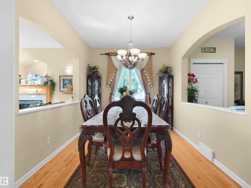 Wood-finish flooring throughout, complemented by a suspended chandelier and arched wall openings - 614 Silver Berry Road Nw, Edmonton, AB - Indoor Photo Showing Dining Room