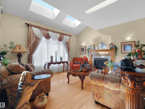 Vaulted ceiling with dual skylights, light wood-finish flooring, and a fireplace with a wood mantel - 614 Silver Berry Road Nw, Edmonton, AB - Indoor Photo Showing Living Room With Fireplace