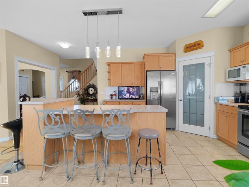 Kitchen featuring stainless steel appliances, wood-finish cabinetry, tile flooring, and a central island with bar seating - 614 Silver Berry Road Nw, Edmonton, AB - Indoor