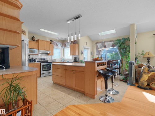 Open-concept kitchen with wood cabinetry, stainless steel appliances, and a tiled floor - 614 Silver Berry Road Nw, Edmonton, AB - Indoor Photo Showing Kitchen