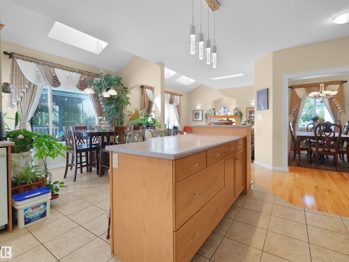 Kitchen island with integrated storage, tile flooring, pendant lighting, skylights, and a dining area with large windows - 614 Silver Berry Road Nw, Edmonton, AB - Indoor