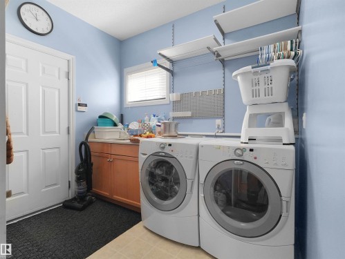 Built-in cabinetry with light-colored countertops, window with blinds, and wall-mounted shelving - 614 Silver Berry Road Nw, Edmonton, AB - Indoor Photo Showing Laundry Room
