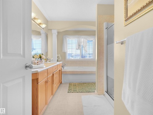 Dual vanity with wood-finish cabinetry, built-in bathtub, glass-enclosed shower, and tile flooring - 614 Silver Berry Road Nw, Edmonton, AB - Indoor Photo Showing Bathroom