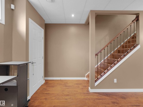 Wood-finish flooring with white trim, a staircase featuring wrought iron balusters and wood handrail, and a drop ceiling with recessed lighting - 614 Silver Berry Road Nw, Edmonton, AB - Indoor Photo Showing Other Room
