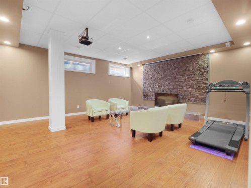 Wood-finish flooring throughout, featuring a stone accent wall with a built-in fireplace, drop ceiling with recessed lighting, and a mounted projector - 614 Silver Berry Road Nw, Edmonton, AB - Indoor Photo Showing Gym Room
