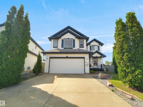 Two-story residence featuring white siding with dark trim, a double garage, front porch with columns, and mature landscaping - 614 Silver Berry Road Nw, Edmonton, AB - Outdoor With Facade