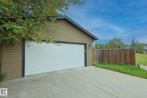 Attached garage with horizontal siding, a paneled garage door, concrete driveway, and a wood privacy fence - 11739 129 Street Nw, Edmonton, AB 