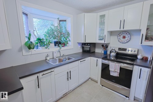 Bay window above a double basin sink, white cabinetry with matte black hardware, dark countertops, and stainless steel appliances - 11739 129 Street Nw, Edmonton, AB 