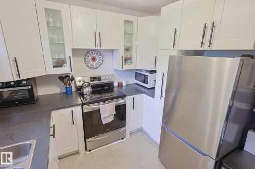 White shaker-style cabinetry with matte black hardware, stainless steel appliances, dark countertops, and light-toned flooring - 11739 129 Street Nw, Edmonton, AB 