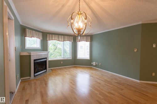 Recessed fireplace with tile surround, wood-finish flooring, multiple windows, and decorative ceiling fixture - #204 2420 108 St Nw, Edmonton, AB - Indoor Photo Showing Other Room With Fireplace