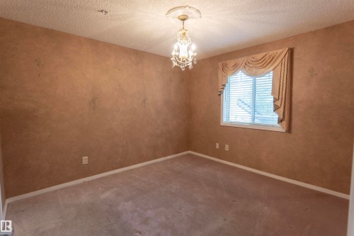 Textured wall finish, ceiling-mounted chandelier, window with blinds, and wall-to-wall carpeting - #204 2420 108 St Nw, Edmonton, AB - Indoor Photo Showing Other Room