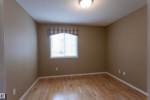 Warm neutral wall tones, wood-finish flooring, and a flush mount ceiling light - #204 2420 108 St Nw, Edmonton, AB - Indoor Photo Showing Other Room