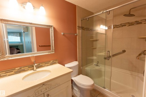Bathroom featuring a single vanity with an integrated sink, decorative framed mirror, and a walk-in shower with a glass enclosure and rain shower head - #204 2420 108 St Nw, Edmonton, AB - Indoor Photo Showing Bathroom