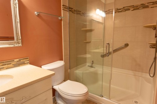 Bathroom featuring a vanity with an integrated sink, decorative mirror, toilet, and a combined tub and shower with a glass enclosure - #204 2420 108 St Nw, Edmonton, AB - Indoor Photo Showing Bathroom