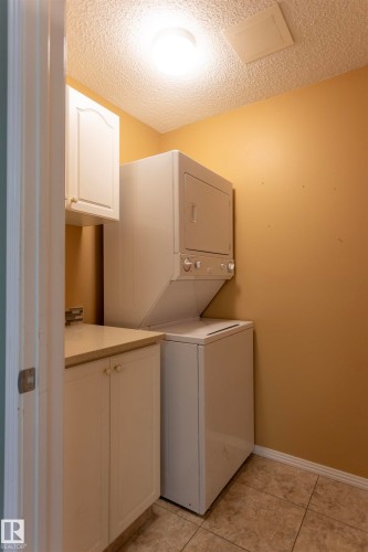 Dedicated laundry room featuring stacked washer/dryer unit, ample cabinetry with countertop workspace, tile flooring, and warm neutral wall finishes - #204 2420 108 St Nw, Edmonton, AB - Indoor Photo Showing Laundry Room
